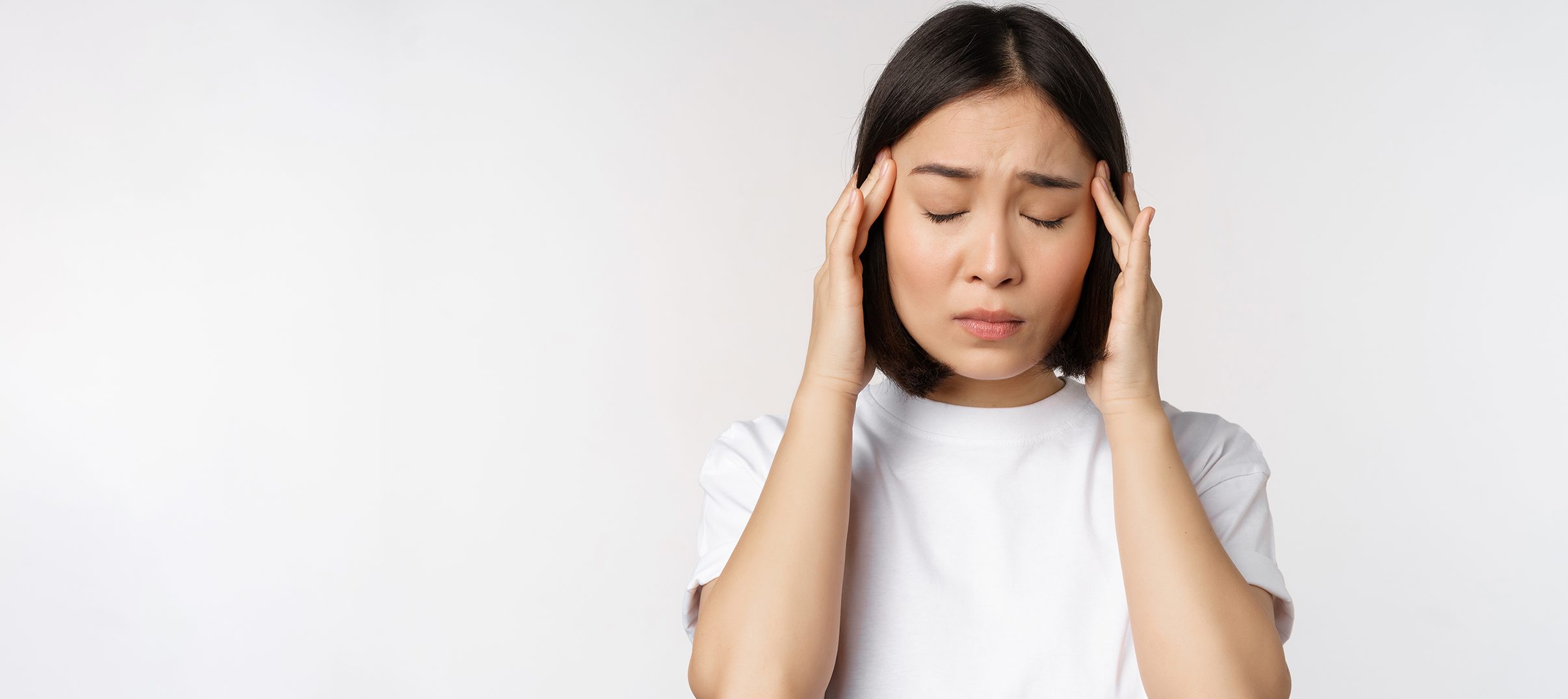 Young woman with short dark hair, eyes closed, pressing her temples as if stressed—perhaps searching for lunetterie à Montréal or the plus grand inventaire de montures à Montréal—against a plain white background.