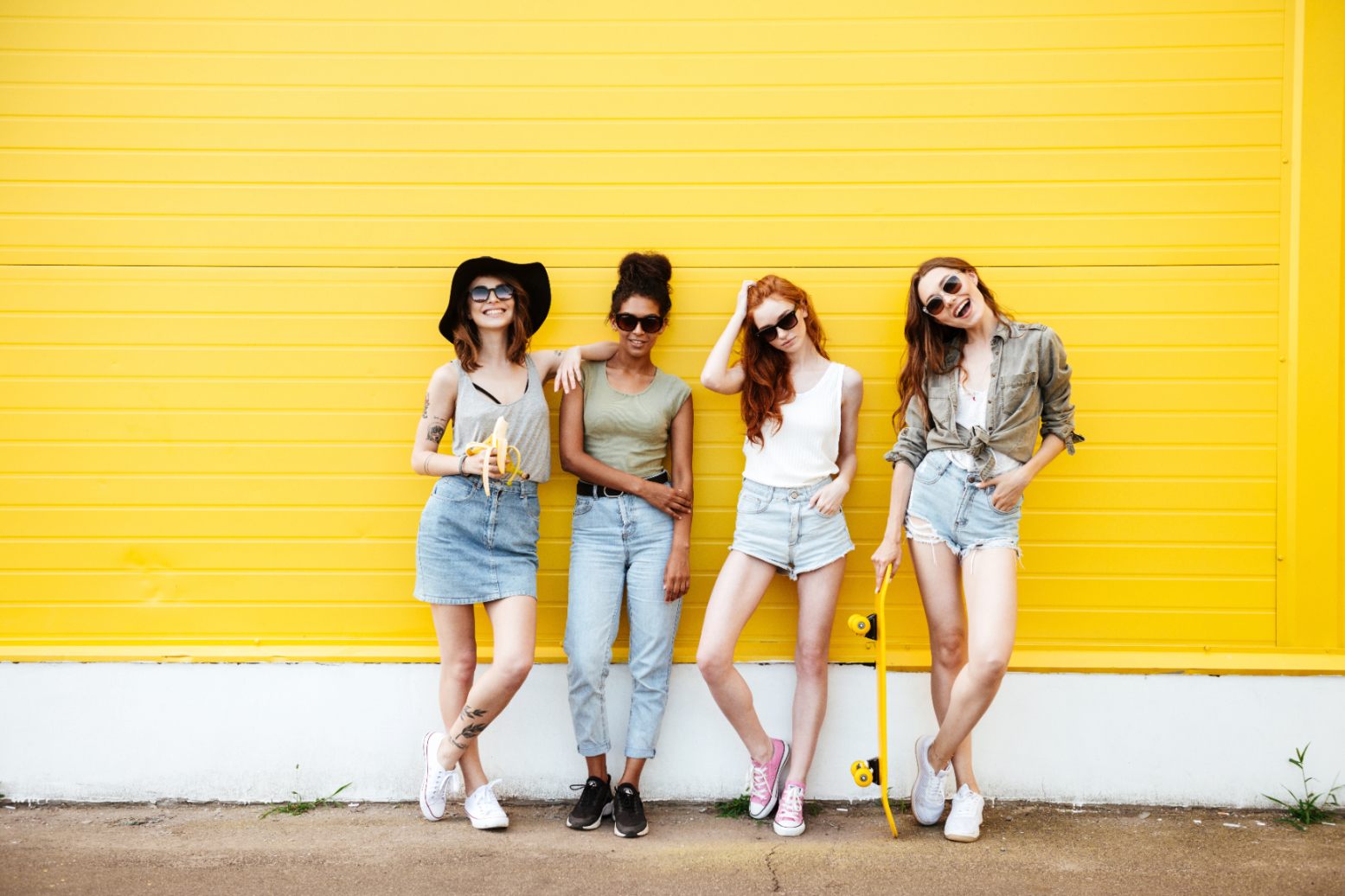 Young smiling women friends standing over yellow wall