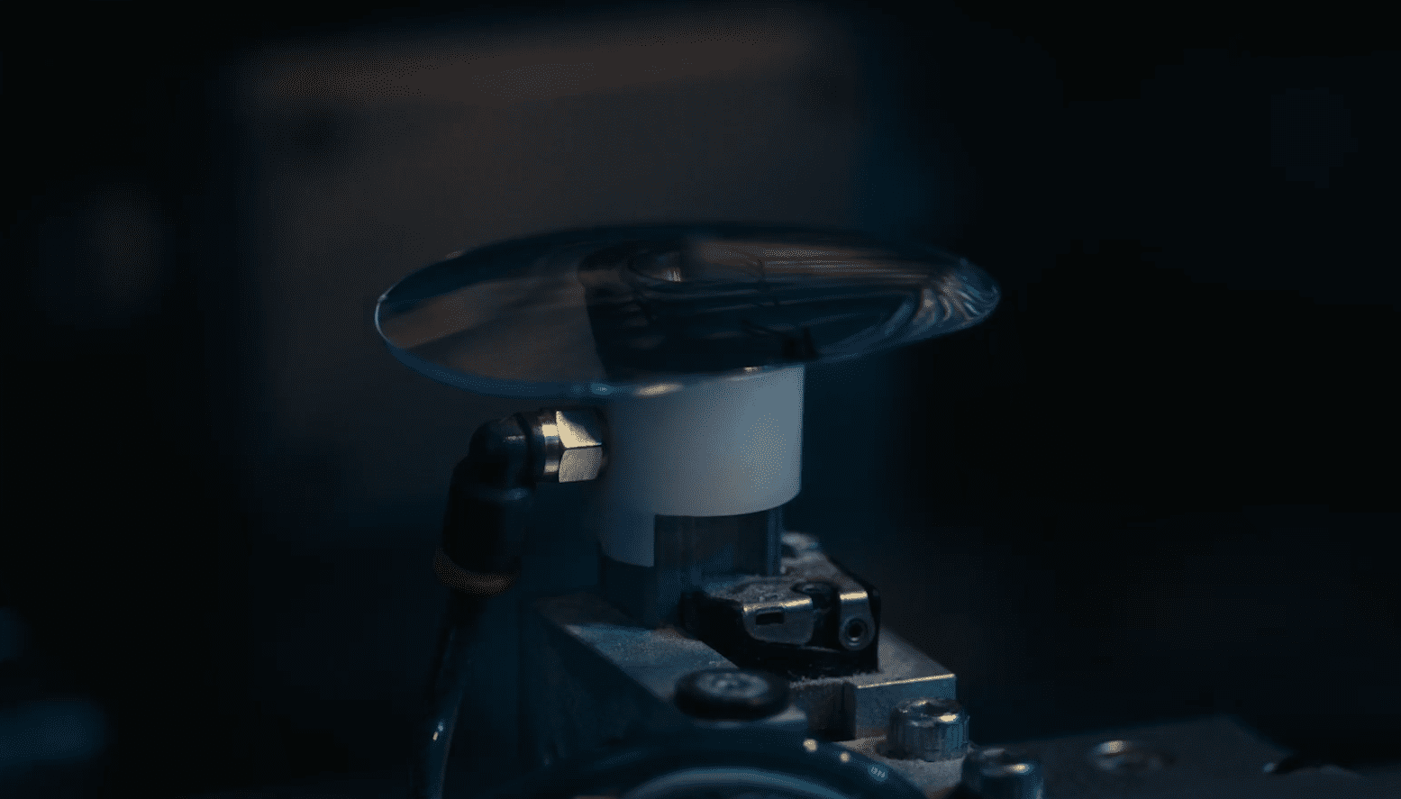 A close-up of a spinning glass disc or lens mounted on a metal apparatus, with a dimly lit background—showcasing the precision found in la lunetterie à Montréal, Vu, where mechanical components are expertly crafted beneath it.