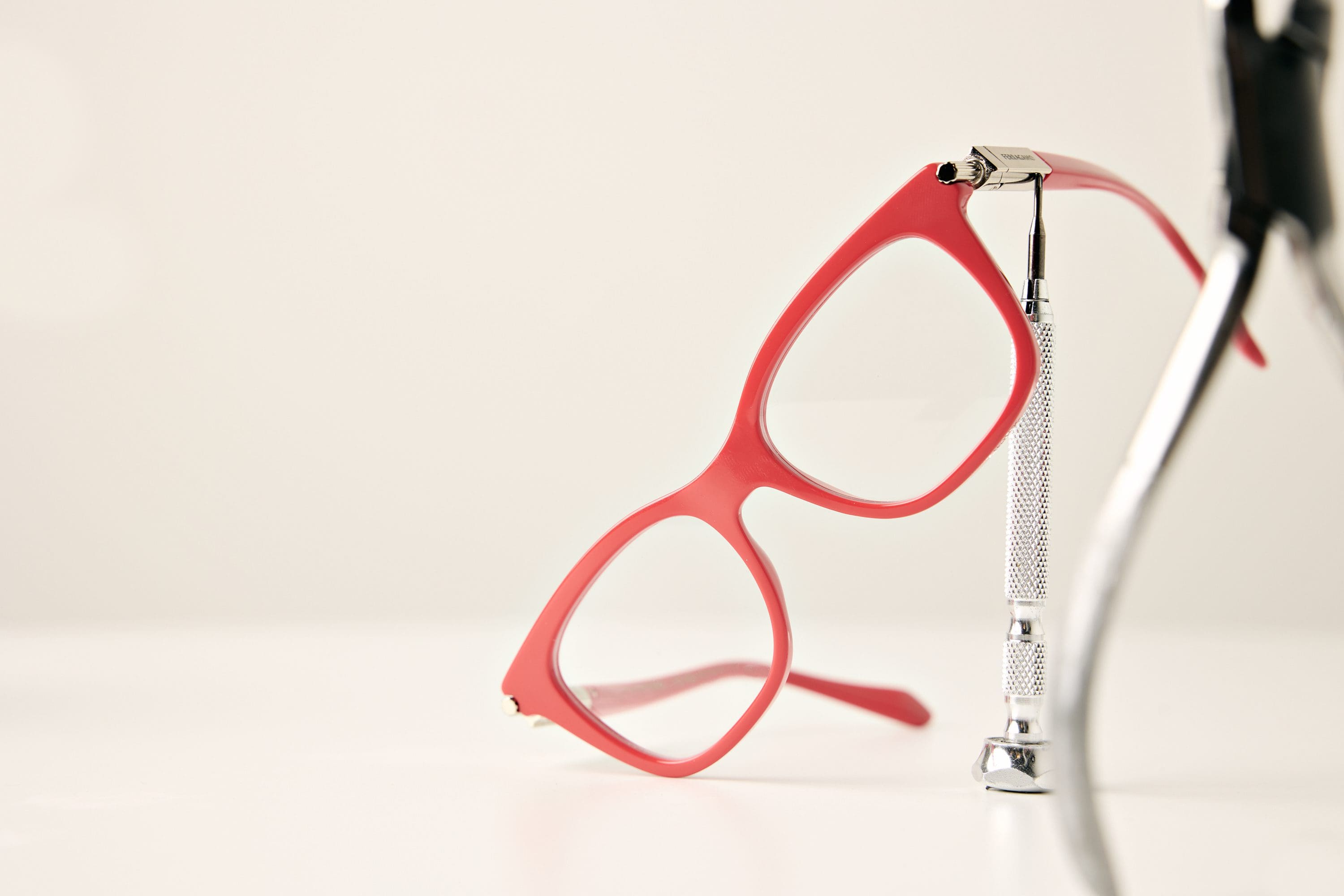 A pair of red eyeglasses from Vu is propped up by a silver optometry tool on a white surface, highlighting the style found at la lunetterie à Montréal.