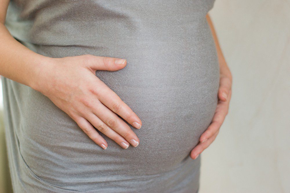 A close-up of a person wearing a gray shirt gently cradling their pregnant belly with both hands, capturing a tender moment at Vu, la lunetterie à Montréal.